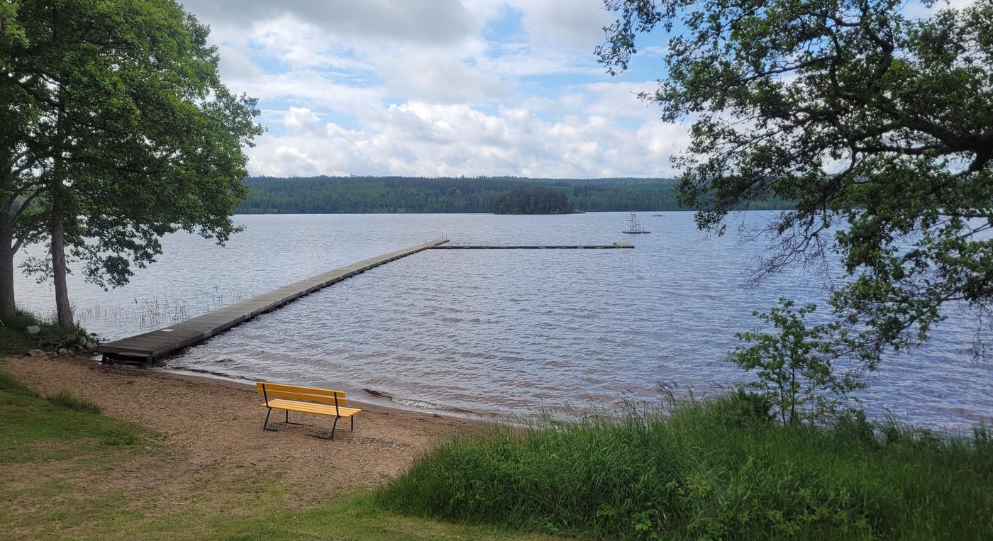 En lång brygga går ut från strandkanten. På en liten flotte syns ett hopptorn.