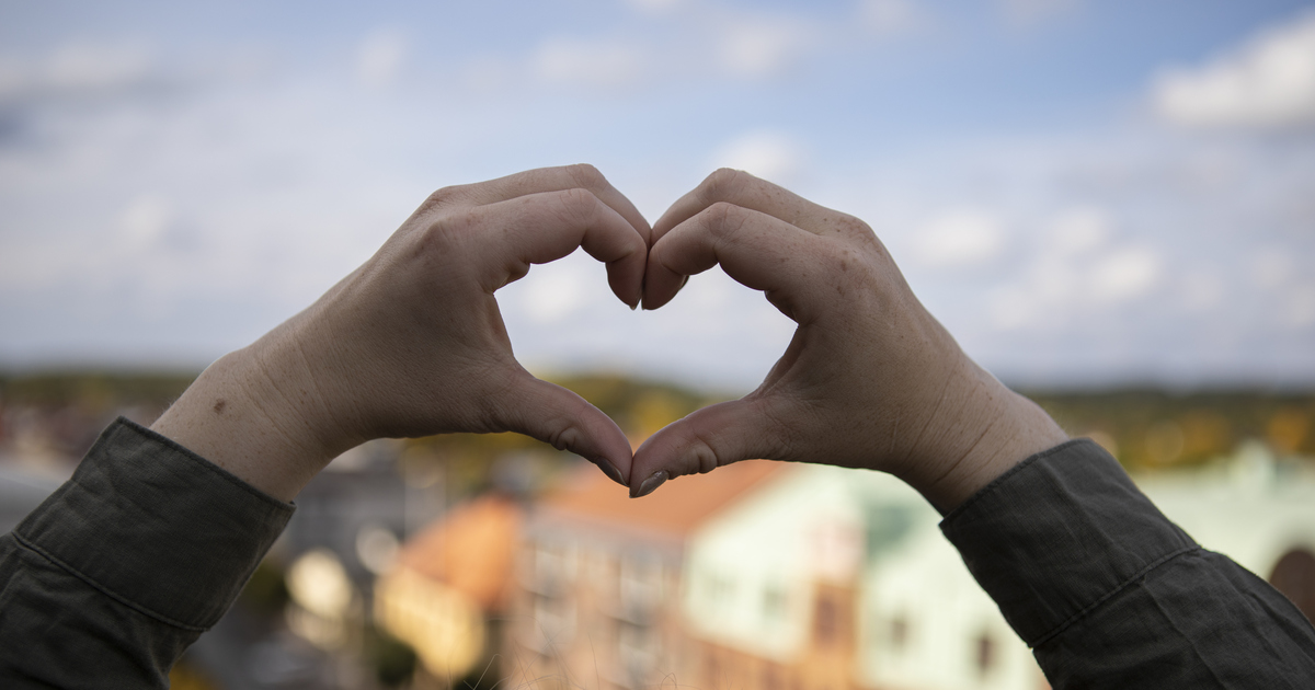 Händer som formar ett hjärta framför Vetlanda stad.