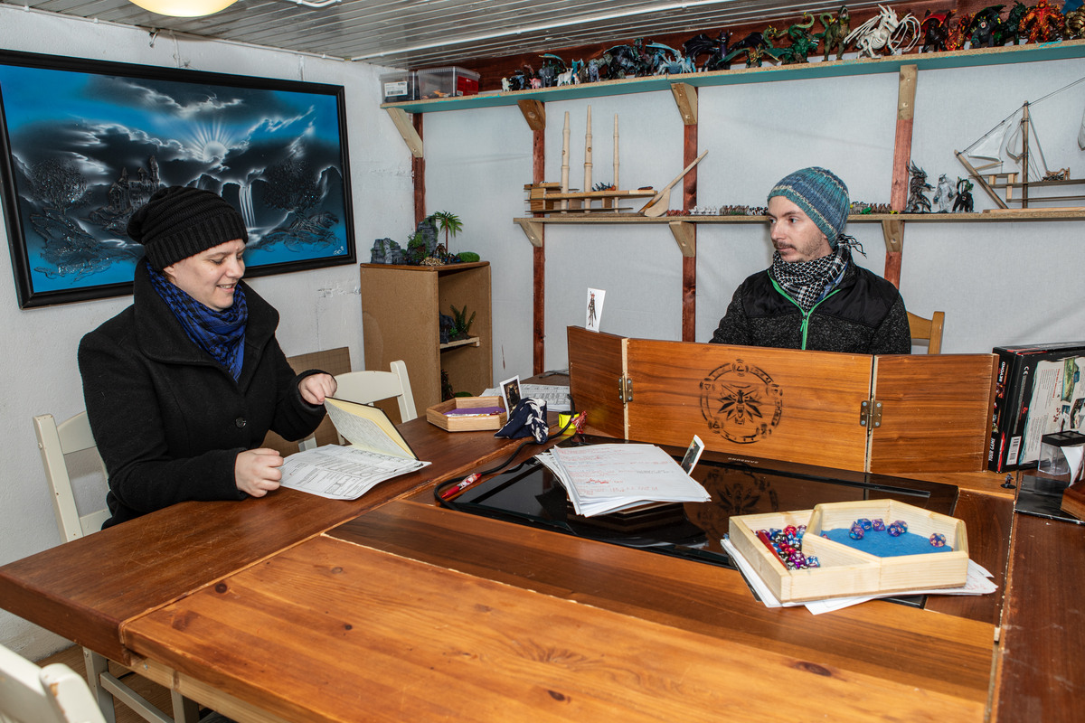 Två personer sitter vid ett stort bord. Den ena personen har skärmar uppbyggda framför sig och föreställer spelledare i spelet Dungeons and Dragons.