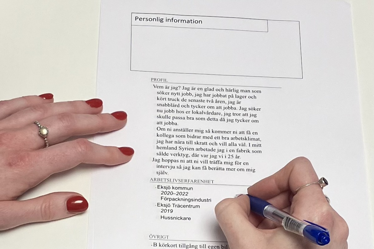 Papper med utskrivet CV och en hand med bläckpenna som skriver på pappret.